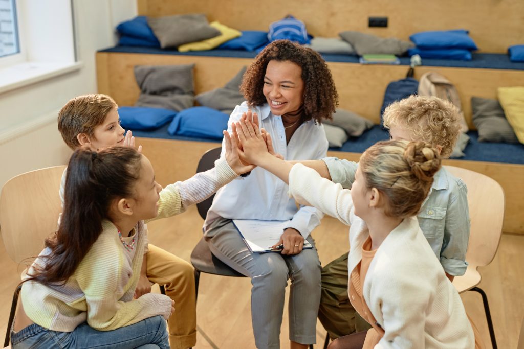 Teacher facilitating a small group of children as they high-five during a classroom activity