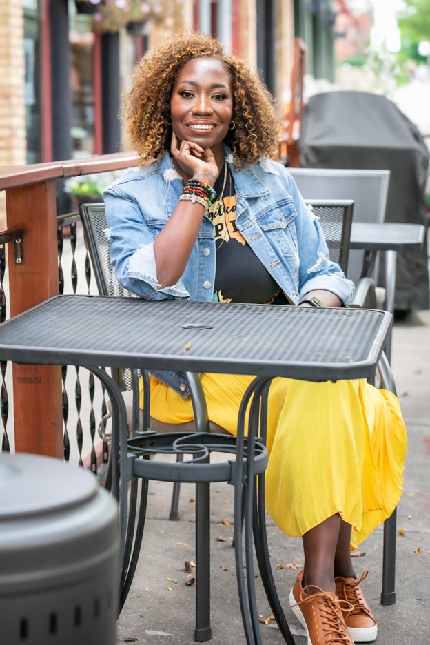 Nedra Cannon, Licensed Clinical Social Worker and keynote speaker, seated in a modern workspace wearing a yellow dress and denim jacket.