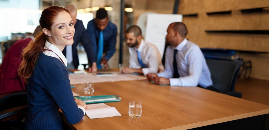 A woman smiling to the camera while working with her business team in a conference room.